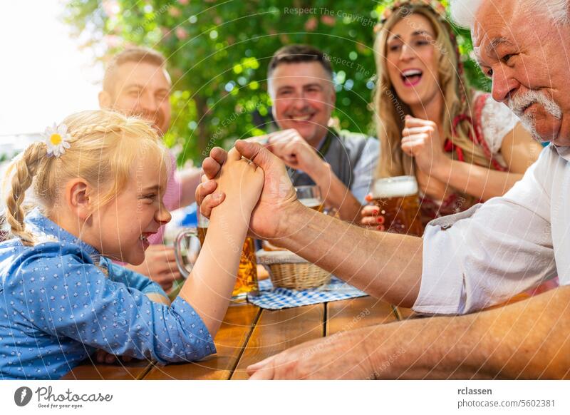 Eine bayerische Familie übt sich in der hohen Kunst des Armdrückens im Biergarten Großvater Tochter Kind Glücksspiel anfeuern Brezeln Spiel Freunde Frau Senior