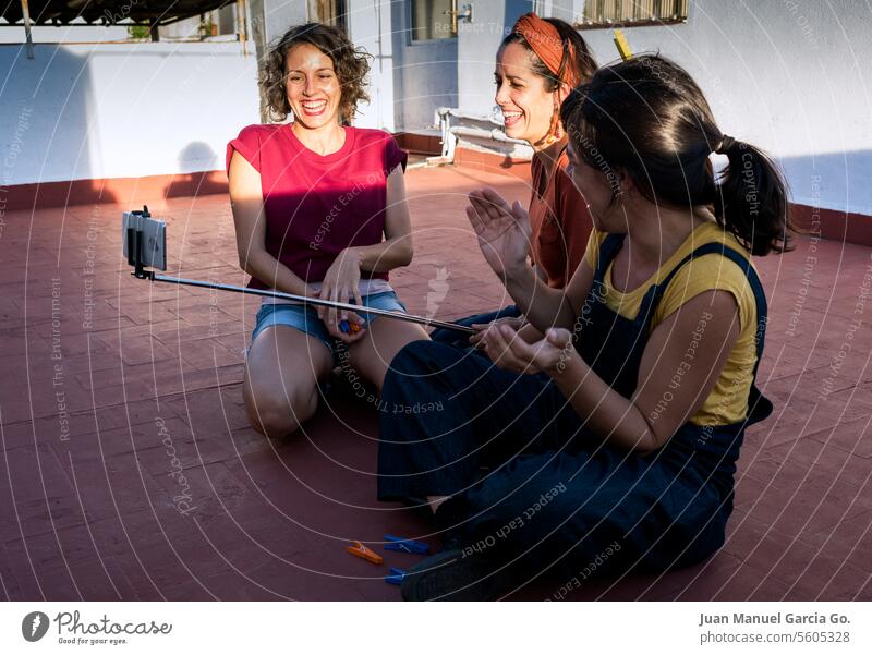 Eine Gruppe von Frauen, die gemeinsam lachen und glückliche Momente erleben, während sie auf einer sonnigen Terrasse ein Selfie machen, um Freundschaft und gute Zeiten zu feiern