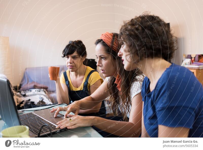 Drei zielstrebige Frauen arbeiten zu Hause an einem Laptop zusammen und verkörpern so die Dynamik eines modernen Remote-Arbeitsteams Teamwork Zusammenarbeit