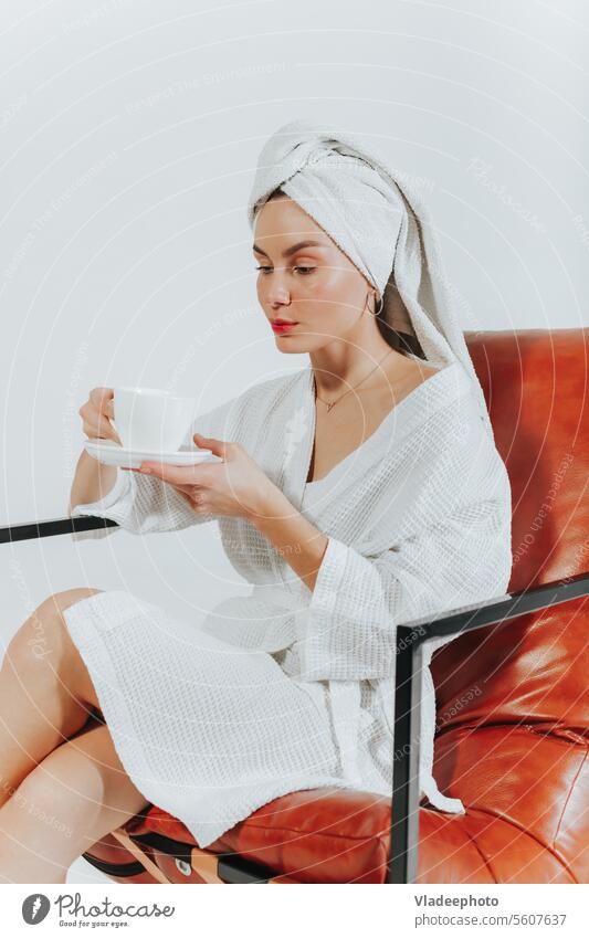 Frau im Bademantel, Kaffee oder Tee trinkend, mit einem weißen Handtuch um den Kopf gewickelt. Weißer Hintergrund Morgen heimwärts Lifestyle Streu Mädchen Dame