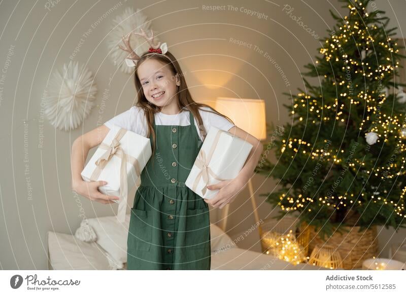 Glückliches Mädchen mit Geschenken und Weihnachtsbaum im Hintergrund Weihnachten präsentieren Feiertag Baum Dekoration & Verzierung Lichter Lächeln Rentier Horn