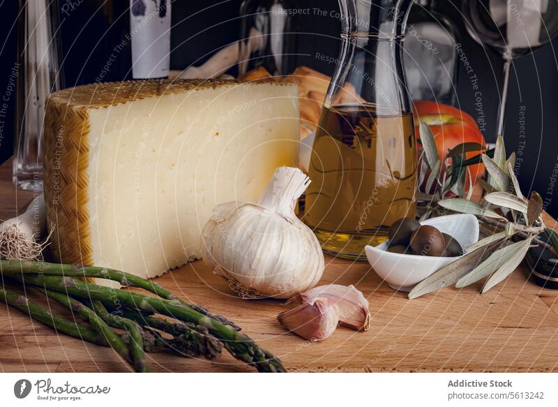 Gourmet-Käse und Zutaten auf einem rustikalen Tisch Handwerklich Knoblauch Spargel Oliven Olivenöl Essensvorbereitung Feinschmecker Lebensmittel