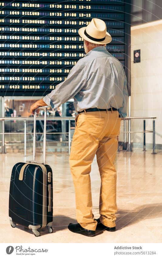 Mann mit Gepäck schaut auf Fahrplan am Flughafen Senior Abheben Holzplatte Zeitplanung Rückansicht Koffer Urlaub reisen in den Ruhestand getreten Lifestyle