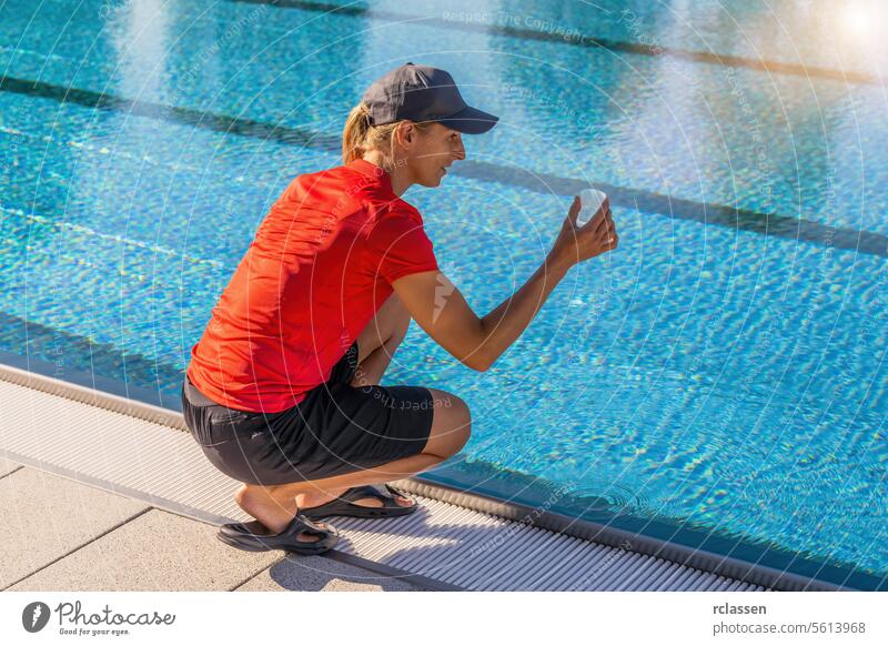 Frau hockt an einem Pool und hält einen durchsichtigen Behälter, um die Wasserqualität in einem Wellness-Resort zu untersuchen Chlor messen Probe Hygiene Sommer