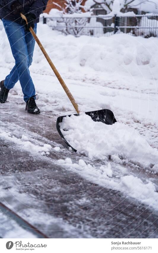 Ein Mann räumt Schnee mit einer Schneeschaufel von einer Strasse Winterdienst Verkehrswege Straße Wetter Schneefall Glätte Wege & Pfade Frost Außenaufnahme