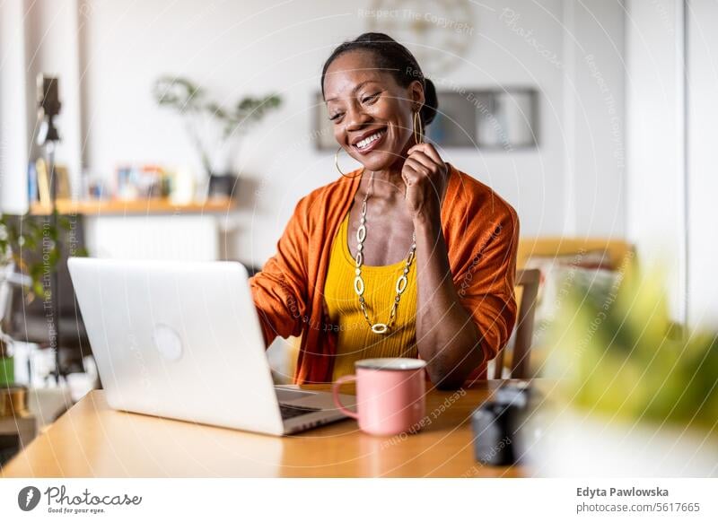 Lächelnde Frau arbeitet zu Hause am Laptop Menschen Freude schwarz natürlich attraktiv schwarze Frau Fröhlichkeit Glück echte Menschen reif Erwachsener