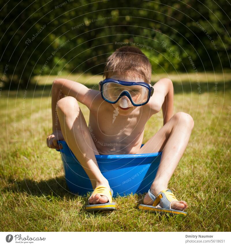 Junge mit Schwimmmaske, der an einem heißen Sommertag in einer Waschschüssel mit Wasser sitzt 7 Jahre Aktivität Kaukasier Kind Kindheit Nahaufnahme Tag