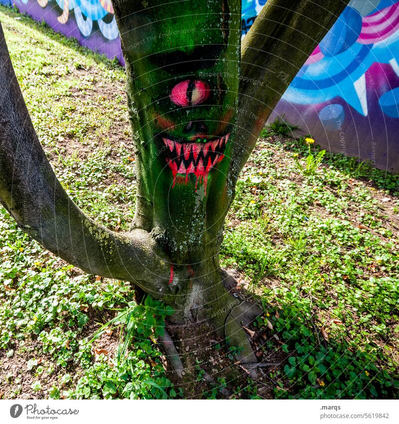 Blutrünstiger Baum im Sonnenschein baumstamm rinde grafitti zeichnung bizarr Monster skurril gruselig Halloween Auge Mund gruseln gefährlich Angst Gesicht Zähne