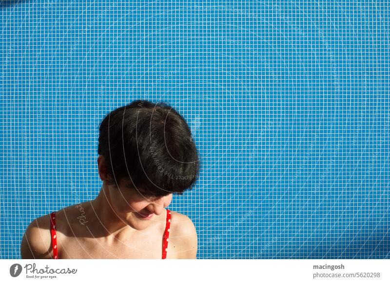 Junge Frau mit schwarzen Haaren vor blauer Fliesenwand im Schwimmbad Innenaufnahme Sonnenlicht Sommer Urlaub Erholung Ferien Schwimmen Baden Mosaik Freizeit