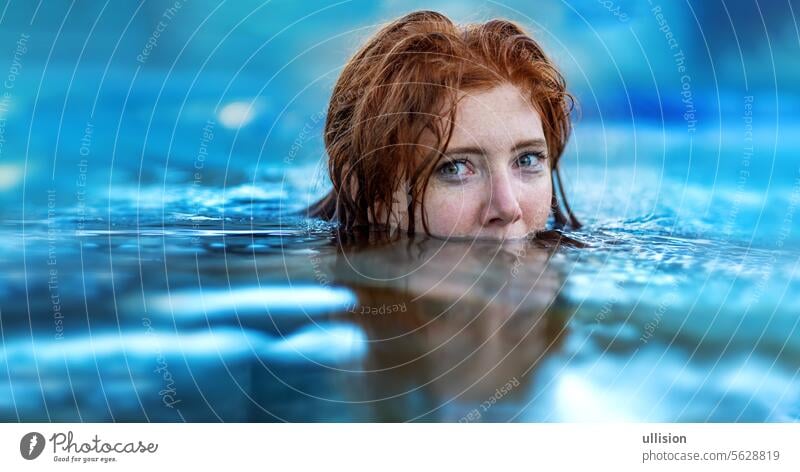 Porträt einer schwimmenden sexy, jungen rothaarigen Frau mit Sommersprossen und rotem, nassem Haar, im türkisfarbenen Spa-Pool-Wasser, Kopf halb unter Wasser