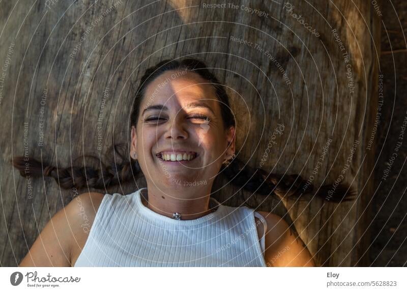 Lächelnde junge Frau, Nahaufnahme einer brünetten Frau mit zwei Zöpfen, die mit geschlossenen Augen lächelnd auf einem Holzstamm liegt Erwachsene 18-30 Jahre