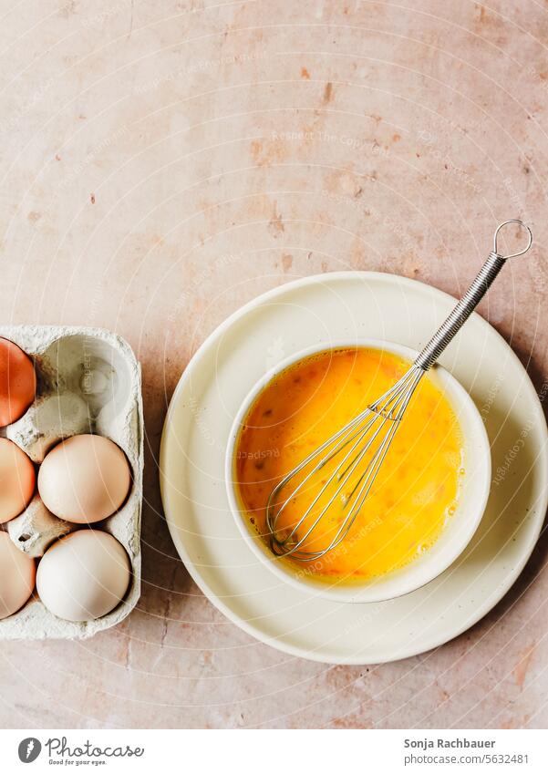 Verührte Eier in einer Schüssel mit einem Schneebesen. Draufsicht. Rührei Vorbereitung Frühstück eier Eierkarton frisch Ernährung Eierschale Diät Protein roh