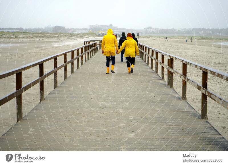 Touristen im gelben Ostfriesennerz bei Sturm und Regenwetter auf der Seebrücke am Strand von St. Peter-Ording im Kreis Nordfriesland in Schleswig-Holstein im Herbst an der Nordseeküste