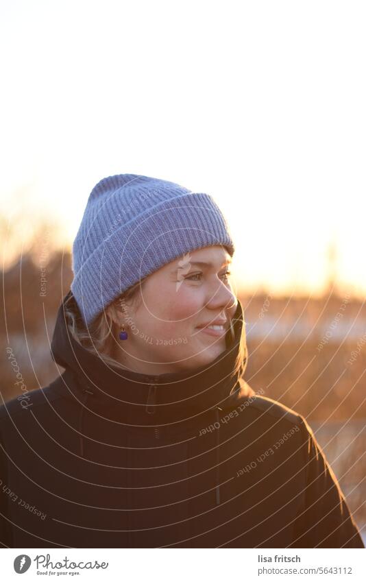 SONNE IM WINTER - GENIESSEN - LÄCHELN Frau 18-30 Jahre blond Mütze blaue Mütze Winter winterjacke Warmes Licht zur Seite schauend Lächeln Erwachsene Farbfoto