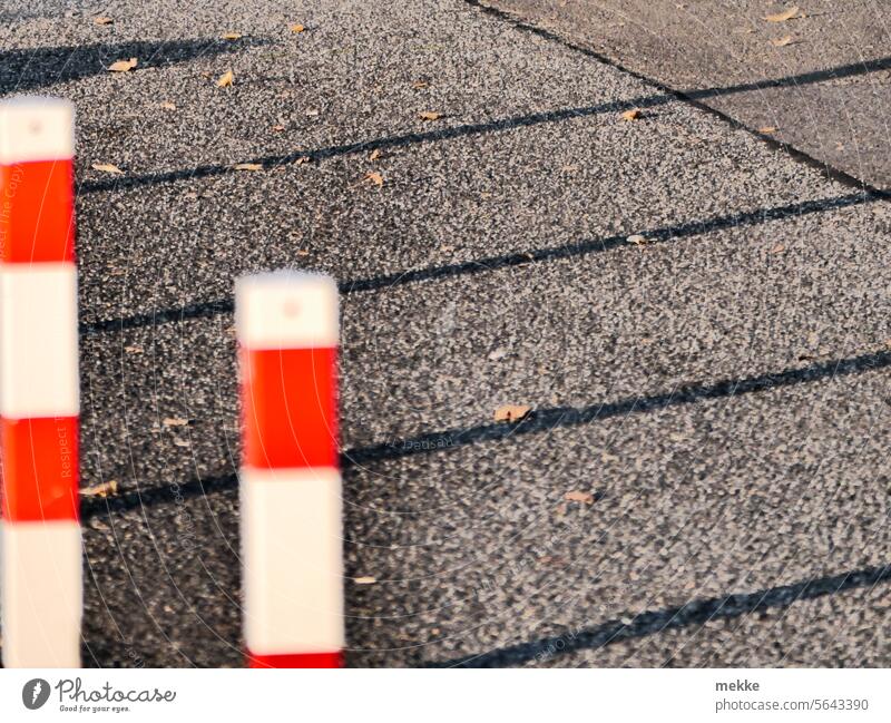 Lange Schatten hinter den Straßenpollern Poller Pfeiler rot weiß Stopp Grenze Begrenzung Barriere Zaun Schutz Sicherheit Asphalt Verbote Absperrung rot-weiß