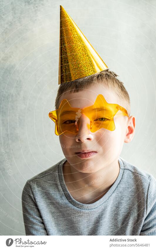 Junge mit Partyhut und sternförmiger Brille auf strukturiertem Hintergrund Neujahrsfest texturierter Hintergrund feierlich golden gelb Sonnenbrille Lächeln jung