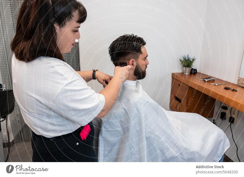 Seitenansicht einer fokussierten Friseurin, die einen elektrischen Trimmer an den Haaren eines männlichen Kunden im Salon benutzt Mann Behaarung Pflege Dienst
