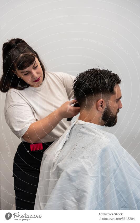 Seitenansicht einer fokussierten Friseurin, die einen elektrischen Trimmer an den Haaren eines männlichen Kunden im Salon benutzt Mann Behaarung Pflege Dienst