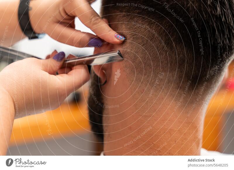 Abgeschnittene, nicht erkennbare Hände einer Friseurin, die das Haar eines männlichen Kunden mit einem Rasiermesser im Salon stylt Gerades Rasiermesser Mann