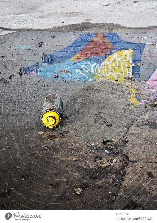 Auf dem Boden eines Lost Places liegt eine leere Spraydose. Ein Streetartkünstler hat sie dort leider liegen lassen. In der Pfütze dahinter spiegelt sich ein Teil seines Kunstwerks.