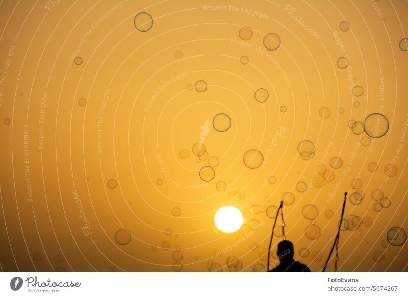 Ein Mann macht viele Seifenblasen mit einem Seifenblasenstab Blasen Wasser abstrakt Regenbogenfarben liquide rund orange Luftblase Air glänzend außerhalb
