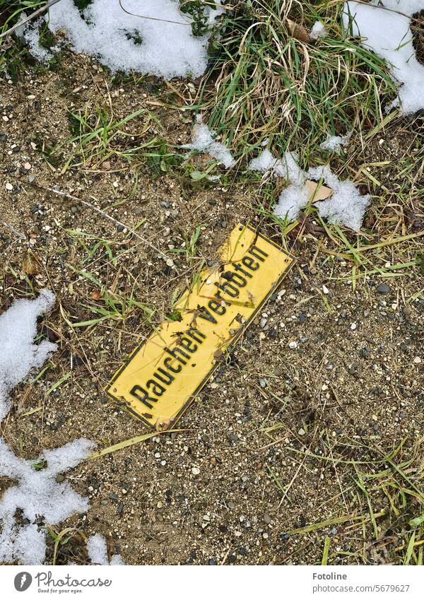 "Rauchen verboten" steht auf dem gelben Schild, dass auf dem kalten verschneiten Boden liegt. Schilder & Markierungen Verbote Hinweisschild Verbotsschild