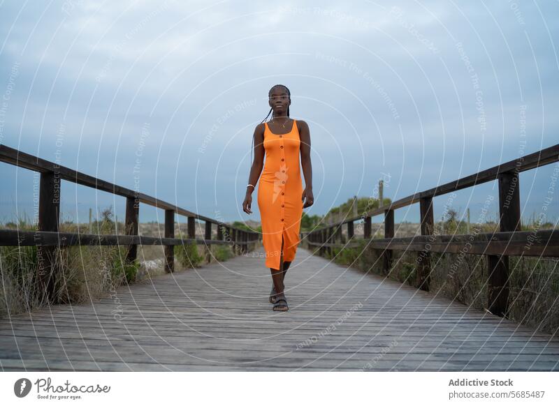 Ernste schwarze Frau, die auf einem Holzsteg geht Spaziergang hölzern Steg Dame Kleid Lächeln positiv Reisender Hügel Berge u. Gebirge Natur reisen Urlaub