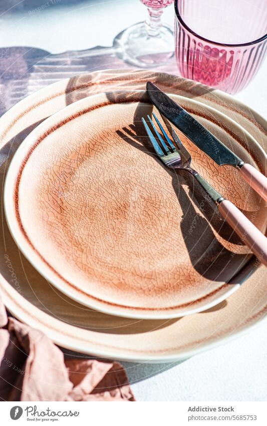 Elegant gedeckter Tisch mit rosa Gläsern Einstellung Teller Keramik Textur Besteck Messer Gabel Glaswaren Schatten Sonnenlicht Eleganz modern speisend Geschirr