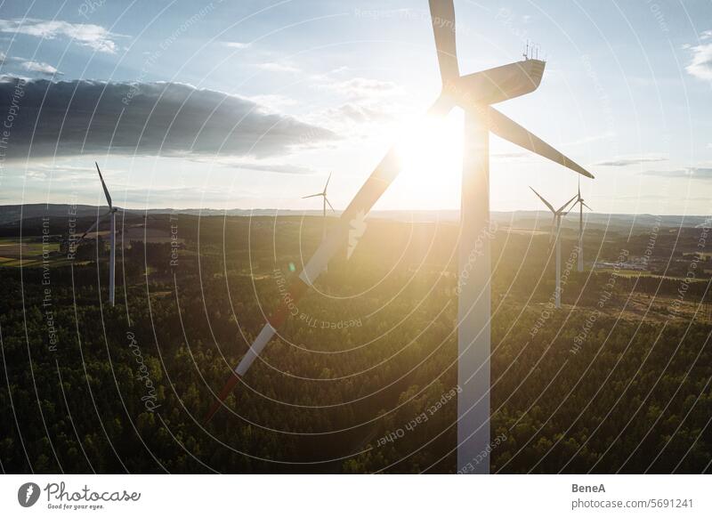 Windkraftanlagen in einem hügeligen Wald vor einem teilweise bewölkten, aber sonnigen Himmel aus der Vogelperspektive bei Sonnenuntergang Antenne Sauberkeit