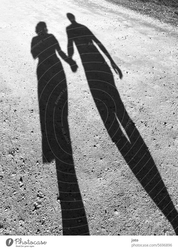 Zwei Personen werfen zwei Silhouetten als Schatten auf den Boden Liebe lieben Paar Händchenhalten händchen haltend händchenhaltend silhouetten Schattenwurf