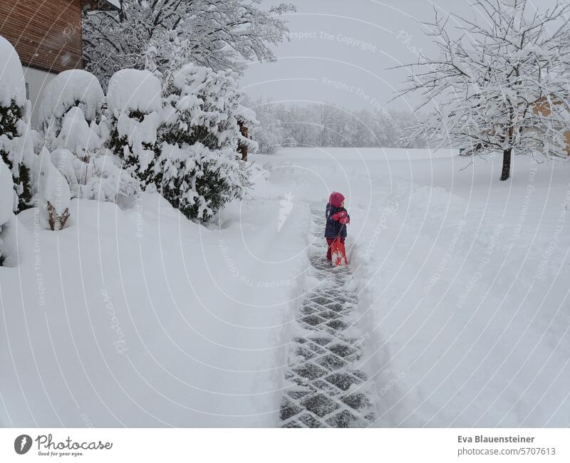Kind mit Schaufel steht auf freigeschaufeltem Weg im Schnee Schneeschaufel Winter Schneesturm schaufeln Schneefall weiß kalt schneebedeckt