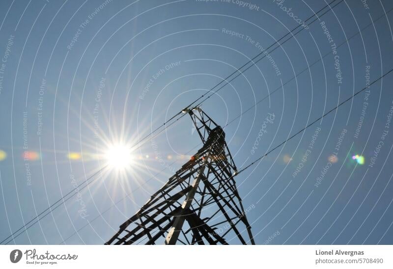 Sehr grafische Komposition mit der Sonne entlang elektrischer Drähte auf der Spitze eines großen Strommastes mit einem blauen Himmel Pylon Elektrizität Draht