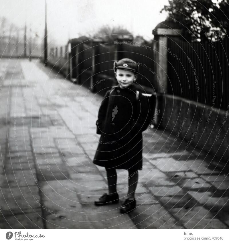 auf dem Schulweg Junge stehen damals früher portrait kleidung Gehweg Bürgersteig Mantel Schulranzen Mauer Straße Blick in die Kamera Mütze Kontrast nostalgie