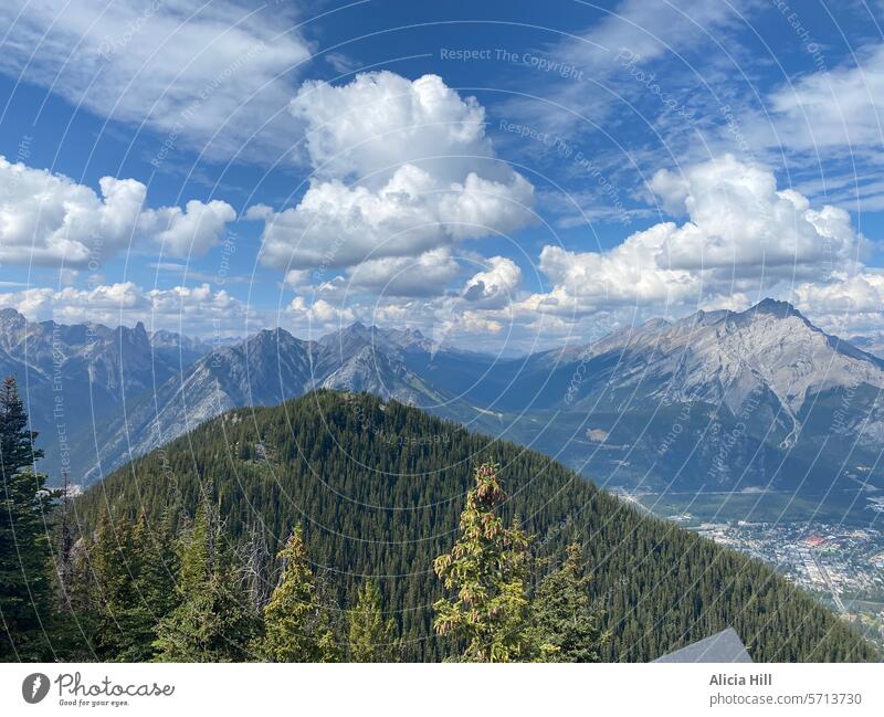 Baumbewachsene Berge im Vordergrund und verschneite Berge im Hintergrund. Strahlend blauer Himmel und flauschige weiße Wolken Berge u. Gebirge Natur