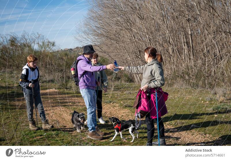 Familienmitglieder mit zwei Hunden auf einer Wanderung, die sich eine Wasserflasche teilen, mit einem jungen Zuschauer, der einen Trekkingstock hält Teilen