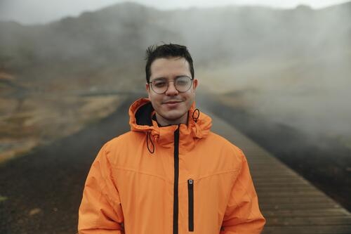 Mann in orangefarbener Jacke genießt neblige isländische Landschaft Island reisen Abenteuer männlich im Freien Nebel orange Jacke Lächeln Brille Promenade Natur