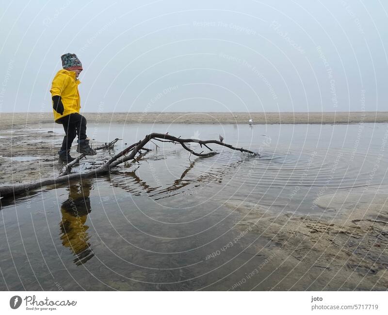 Kind spielt am Strand mit einem Ast an einem nebeligen Tag Herbst herbstlich herbstliche Stimmung grau düster trüb schlechtes Wetter Linien und Formen