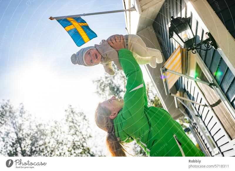 Mutter hebt Baby in die Luft vor einer schwedischen Hütte Eltern Mama Kind Kleinkind Kindheit Schweden Mutterschaft Freude Familie Lächeln Lifestyle Frau Leben