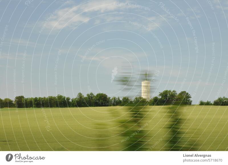 Unscharfer Geschwindigkeitseffekt mit grünen Bäumen durch ein Fenster über Wiesen und einem weißen Silo mit blauem Himmel und wenigen Wolken Feld Unschärfe Baum