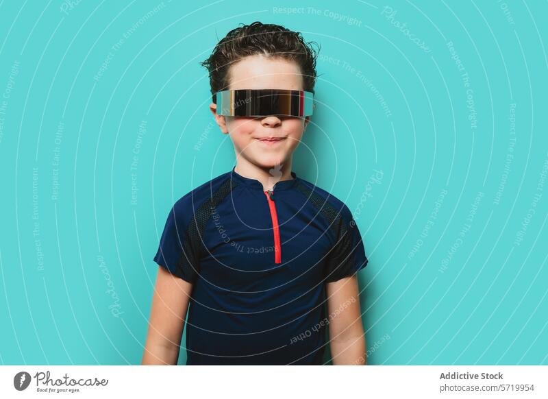 Ein Junge in einem sportlichen Outfit lächelt selbstbewusst, während er eine futuristische Visierbrille vor einem hellen türkisfarbenen Hintergrund trägt visier