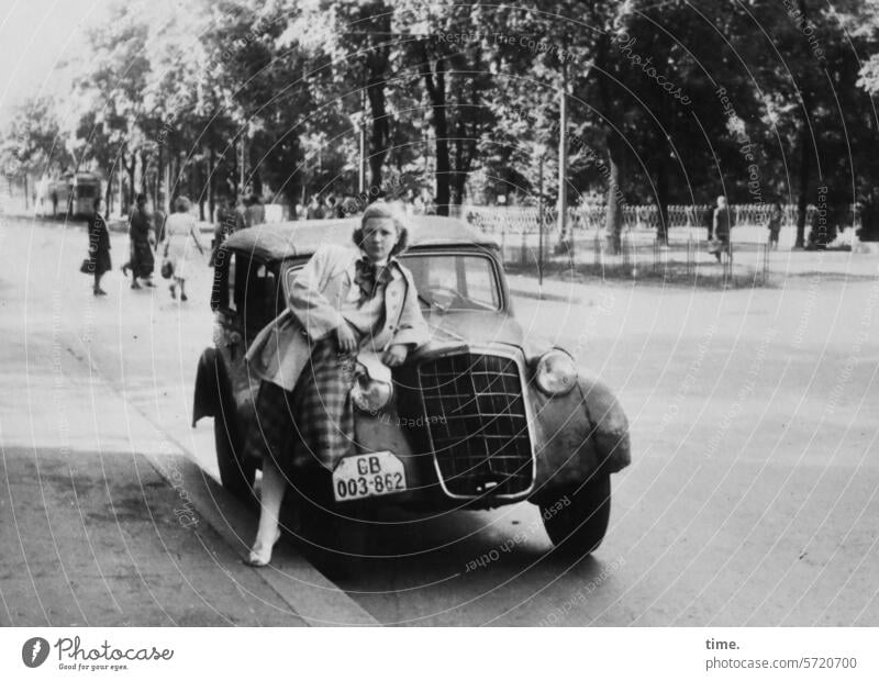 Kühlerfigur Frau Porträt Blick in die Kamera blond Auto Park Straße angelehnt Kraftfahrzeug Straßenverkehr Bürgersteig Bäume Oldtimer posen Traumkarre Mantel