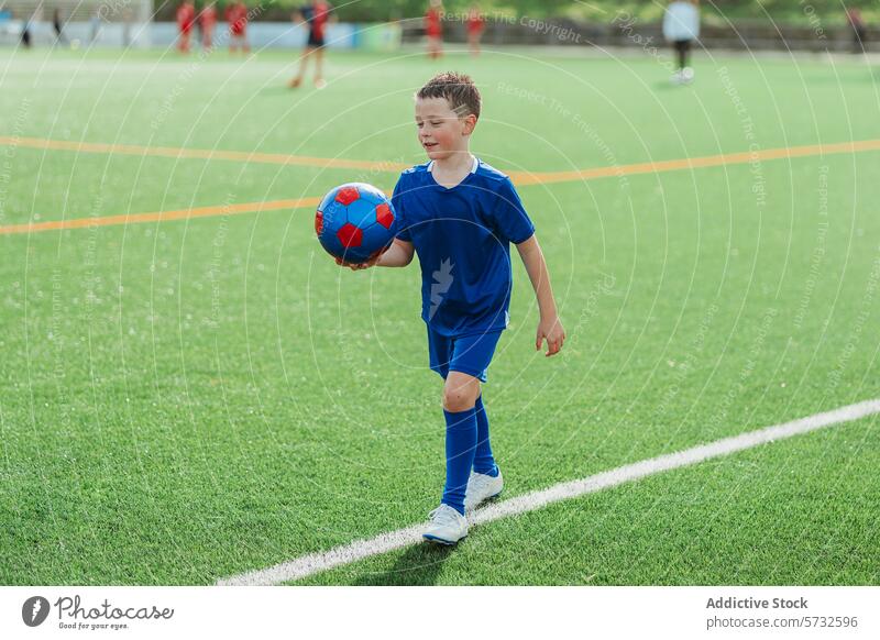 Kleiner Junge in blauer Uniform beim Fußballtraining Kind Ball Sport Freude Spielen Feld Rasen künstlich grün Spaziergang Halt Sportbekleidung Klampen Aktivität