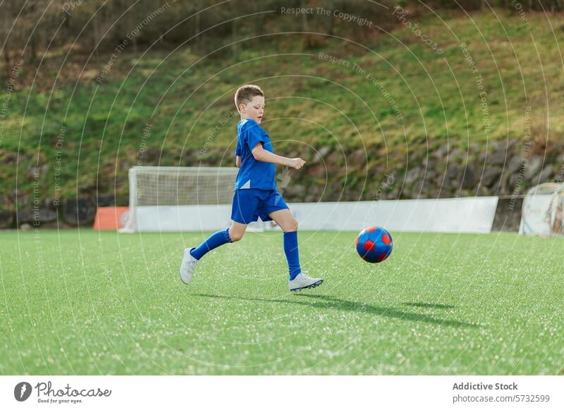 Junger Junge spielt Fußball auf einer grünen Wiese Sport spielen Ball Kick Feld im Freien blau Ausrüstung jung Kind Aktivität sportlich Spiel Jugend Training