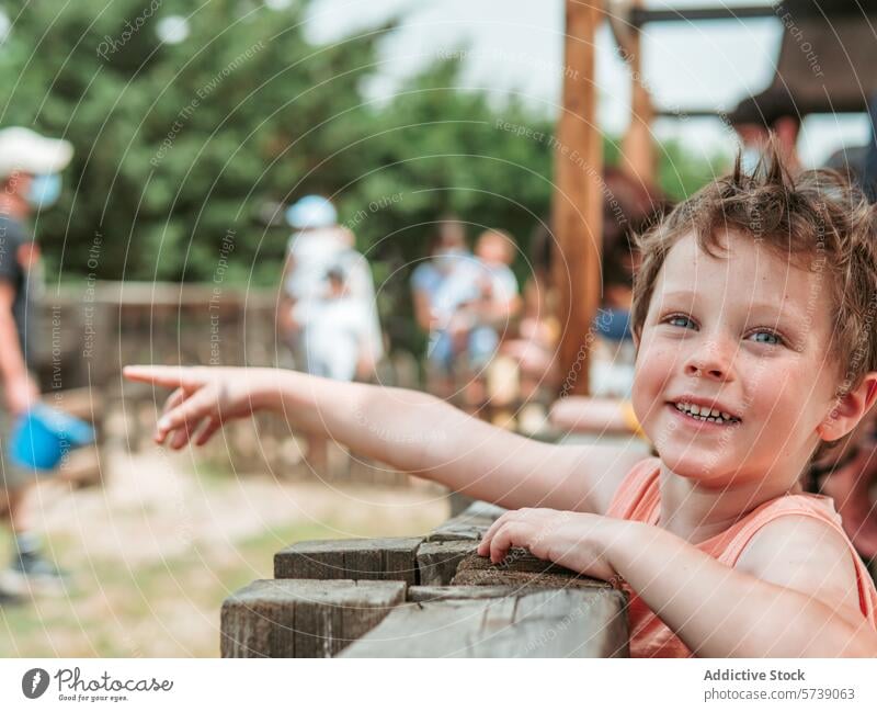 Mit funkelnden Augen und einem freudigen Lächeln zeigt ein kleiner Junge aufgeregt auf etwas, das sich nicht in der Kamera befindet, in einer belebten Schule auf dem Bauernhof