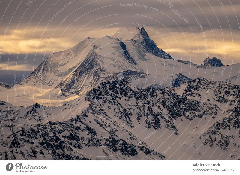 Das warme Licht des Sonnenuntergangs taucht einen majestätischen Alpenberg in ein Licht, das die schneebedeckten Gipfel und das zerklüftete Terrain unter einem dramatischen Himmel hervorhebt