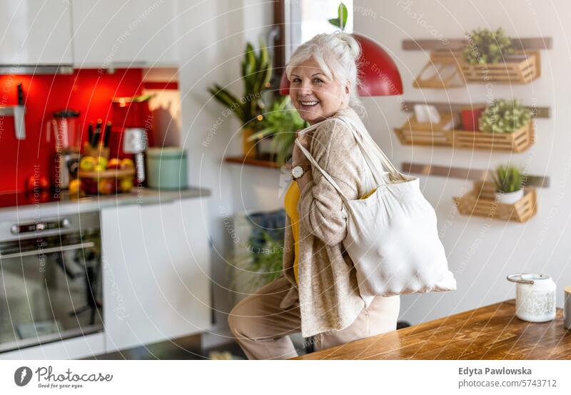 Ältere Frau hält wiederverwendbare Tasche mit Lebensmitteln in der Küche Tisch Einkaufstasche Früchte Gemüse Baumwolltasche Segeltuchtasche Textil