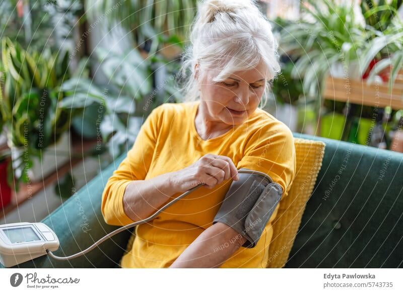 Ältere Frau misst ihren Blutdruck, während sie zu Hause auf einem Sofa sitzt Menschen lässig Tag Porträt im Innenbereich echte Menschen weiße Menschen