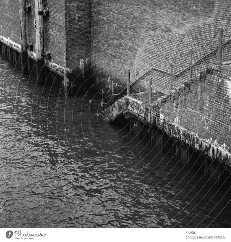 Hamburger Hafenmauer in schwarzweiß Wasser Elbe Fluss Schifffahrt Hafenstadt Stadt Menschenleer Binnenschifffahrt Verkehr Backstein grau dreckig Treppe