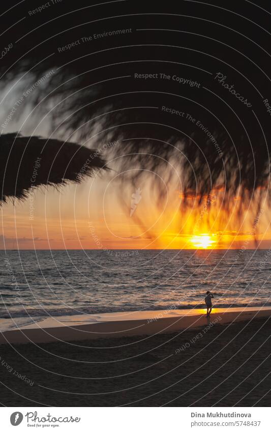 Sonnenuntergang am Meer. Strandurlaub. Vertikale Aufnahme. Strand Sonnenschirme Silhouette. Entfernte Silhouette einer Person zu Fuß am Strand. Urlaub