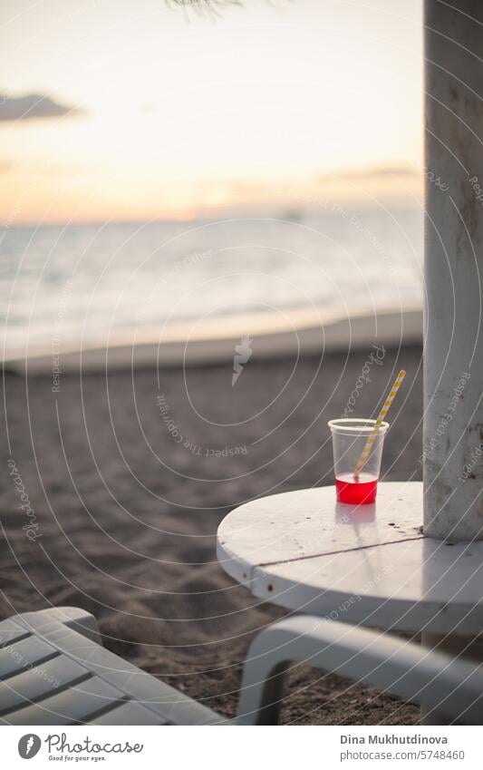 roter Cocktail im Plastikglas am Strandtisch am Meer in der Abenddämmerung nach Sonnenuntergang. Entspannender Urlaub. Sommergetränk. trinken Getränk Sandstrand